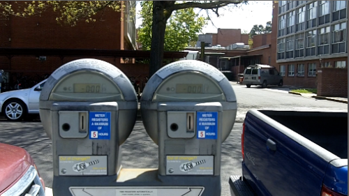 Two Parking Meters right next to each other both flashing "0:00" simultaneously, while the cars for both meters are still visible